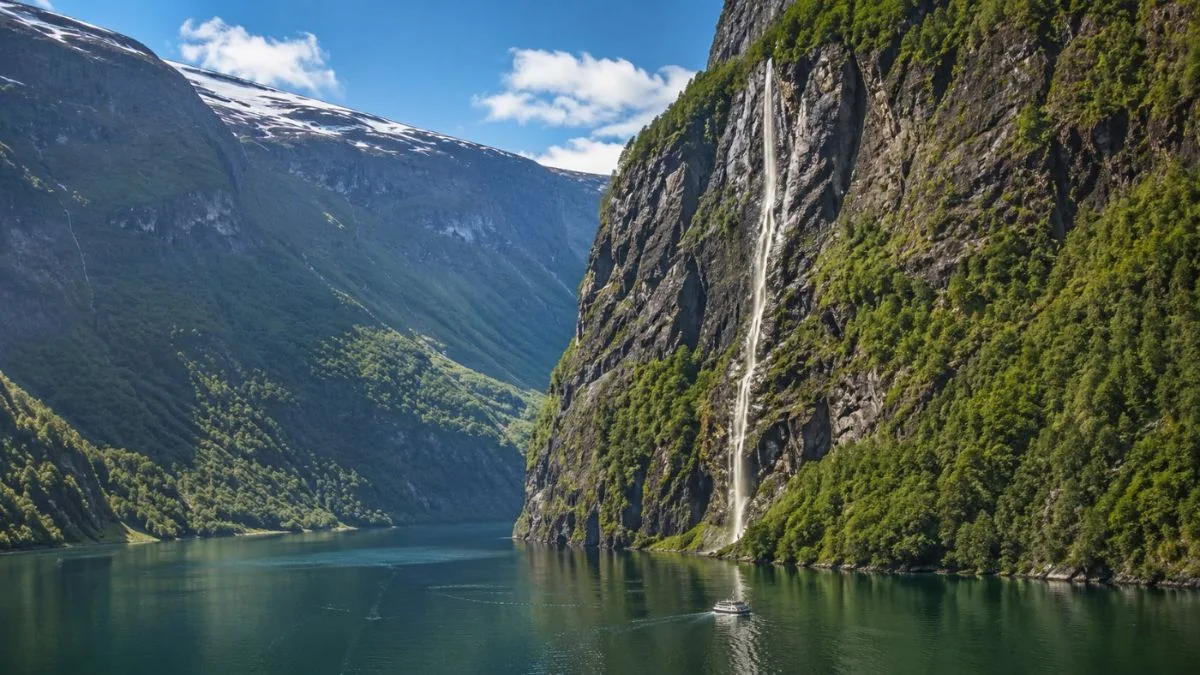 Ein steiler grüner westlicher Fjord mit einem Wasserfall und einem kleinen Kreuzfahrtschiff